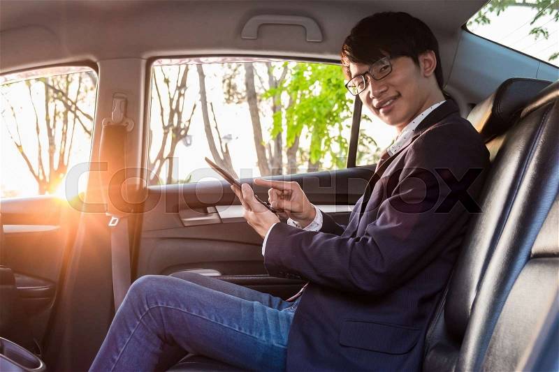 Young handsome businessman working in back of car and using a tablet or smart phone, stock photo