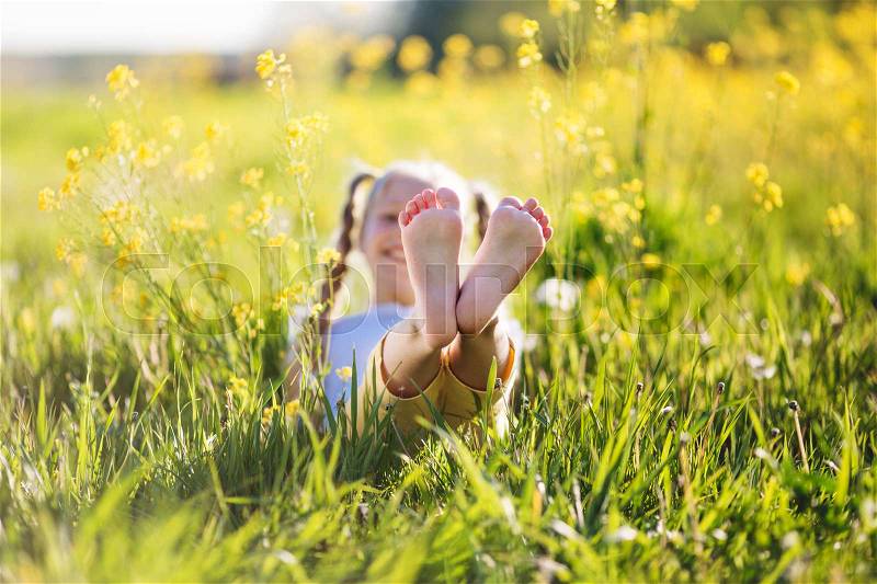 Feet of little cute blonde girl is having fun in yellow field with flowers, stock photo