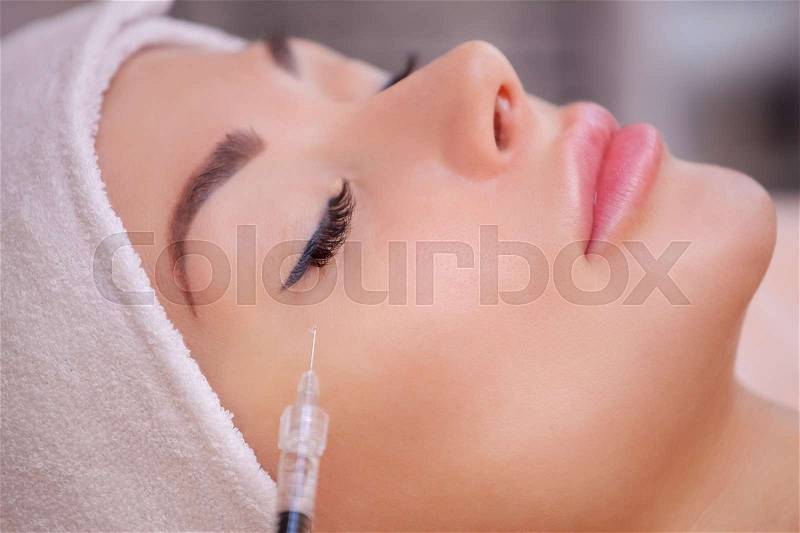 The doctor cosmetologist makes the Botulinotoxin injection procedure for tightening and smoothing wrinkles on the face skin of a beautiful, young woman in a beauty salon.Cosmetology skin care, stock photo