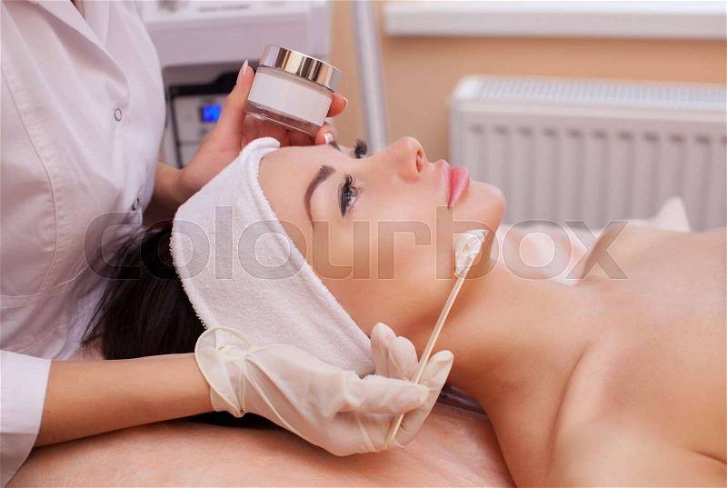 The doctor is a cosmetologist for the procedure of cleansing and moisturizing the skin, applying a mask with stick to the face of a young woman in beauty salon.Cosmetology and professional skin care, stock photo