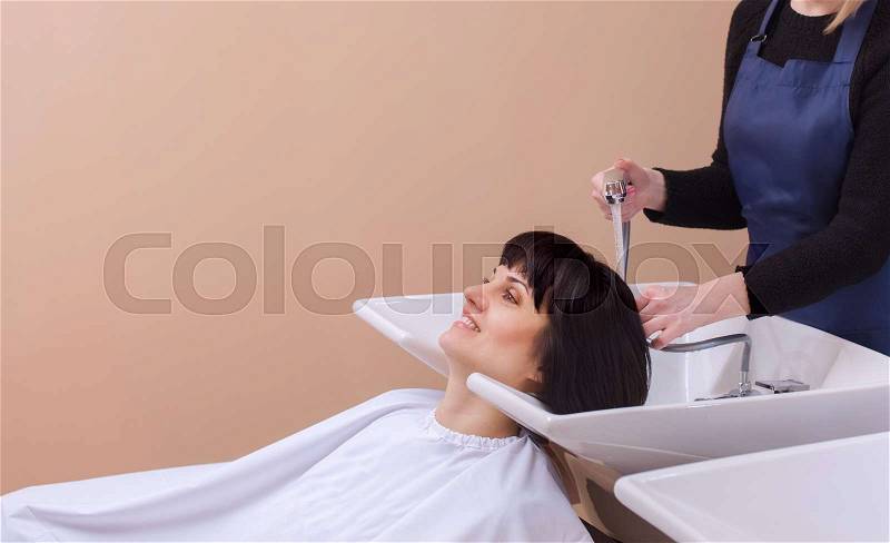 The hairdresser washes the shampoo off the hair to a young girl, brunette in a beauty salon, stock photo