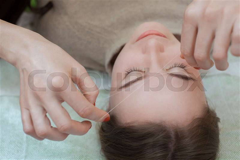 Master corrects makeup gives shape and thread plucks eyebrows in a beauty salon. Professional care for face, stock photo