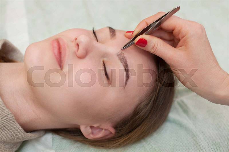 Master makeup corrects, and gives shape to pull out with forceps previously painted with henna eyebrows in a beauty salon. Professional care for face, stock photo