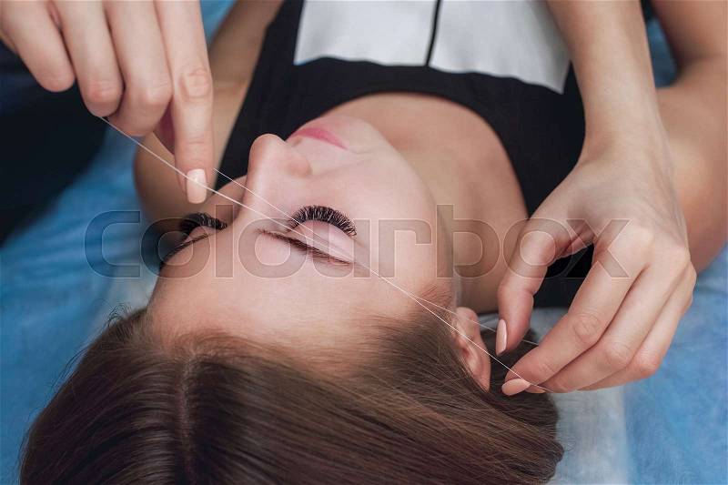 Master corrects makeup gives shape and thread plucks eyebrows in a beauty salon. Professional care for face and eyebrows, stock photo