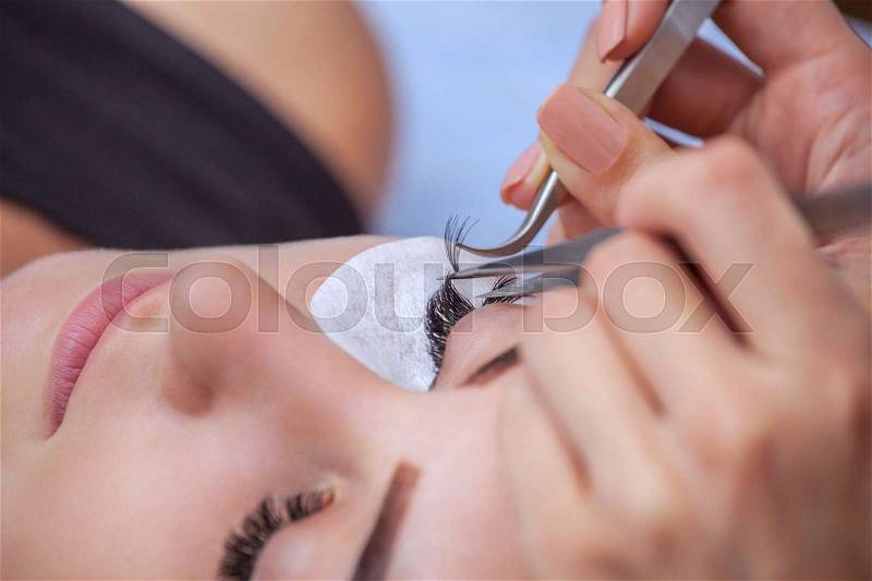 Makeup Master corrects, and strengthens eyelashes beams, holding out a pair of tweezers in a beauty salon. Professional care for the skin and eyes, stock photo