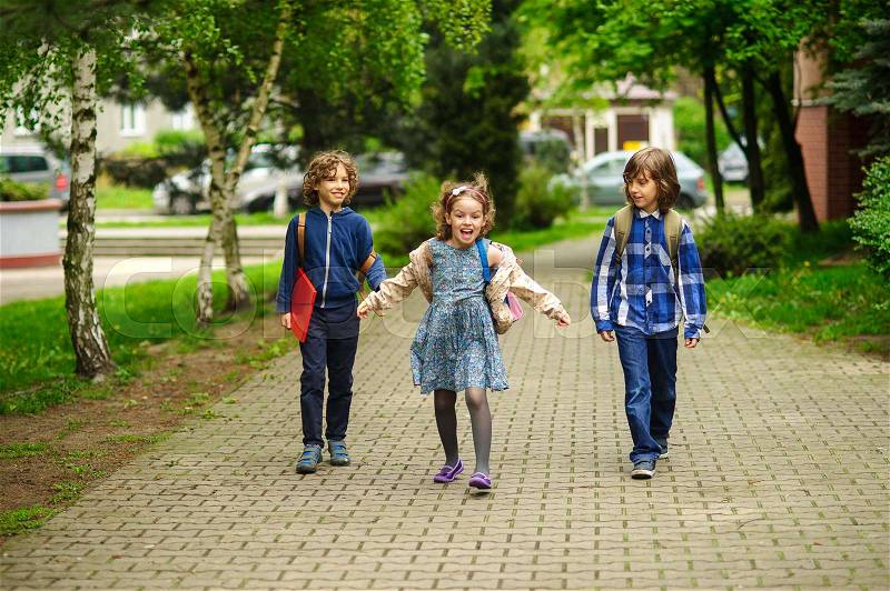 Amusing little school students go to school having joined hands. Children have an excellent mood. Behind shoulders schoolbags. Serene spring day, stock photo