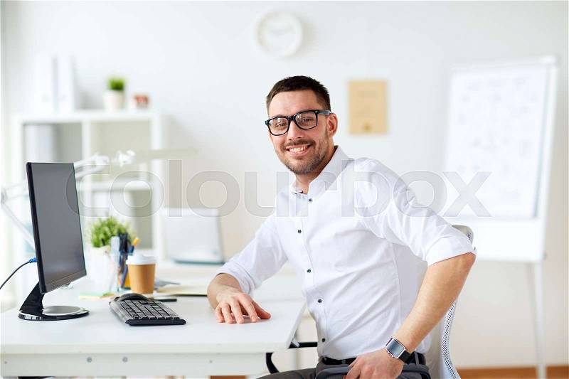 Business, people and technology concept - happy smiling businessman sitting at office computer, stock photo