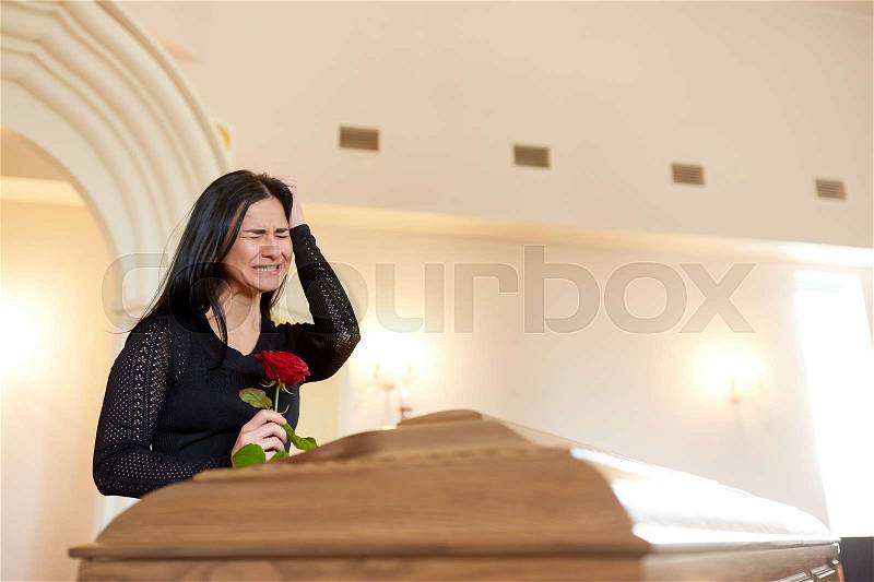 Burial, people and mourning concept - crying unhappy woman with red rose and coffin at funeral in church, stock photo