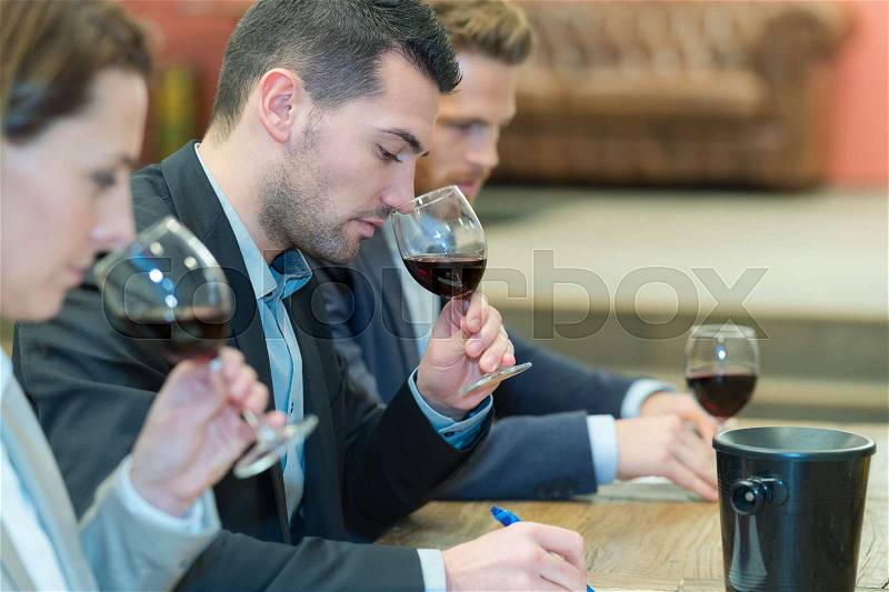 Three people smelling and evaluating red wine in wineglasses, stock photo
