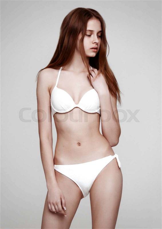 Young beautiful fit fashion model wearing white bikini on grey background, stock photo