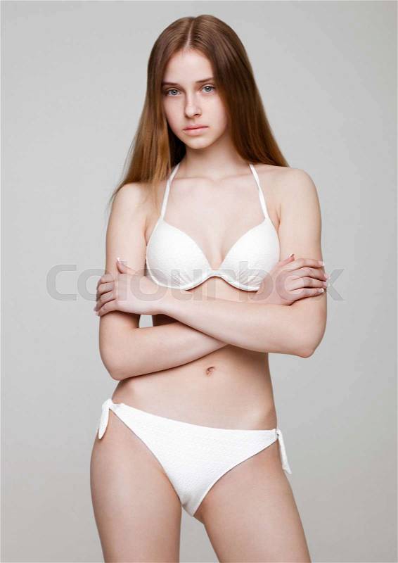 Young beautiful fit fashion model wearing white bikini on grey background, stock photo