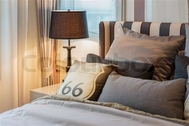 Cozy bedroom interior with dark brown pillows and reading lamp on bedside table, stock photo