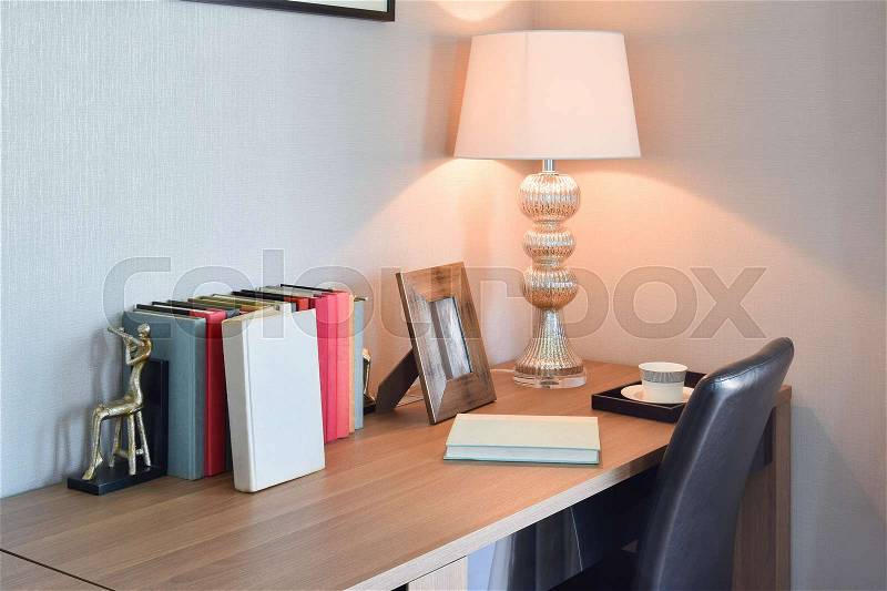 Wooden table with reading lamp and books in modern working room interior, stock photo