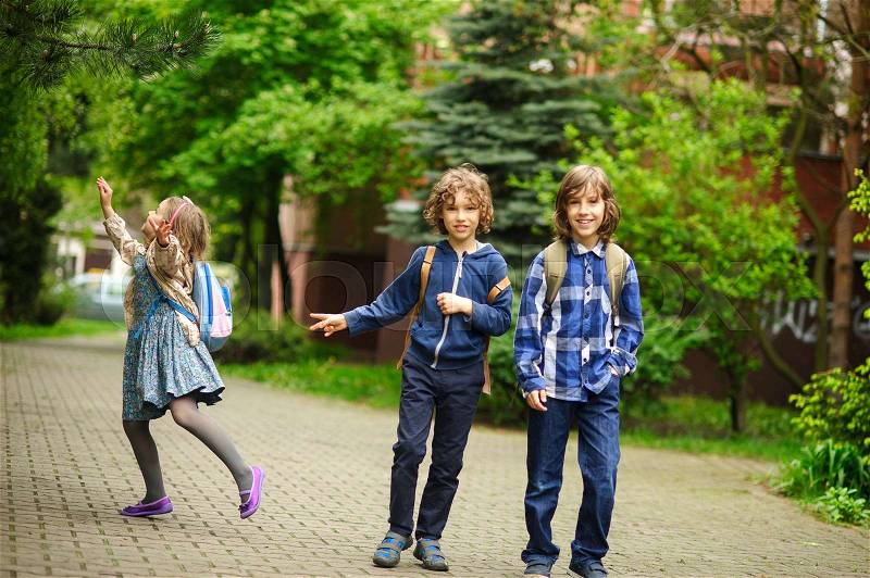 Three little friends hurry on lessons in school. The schoolgirl has noticed something on a tree. Boys smile, stock photo