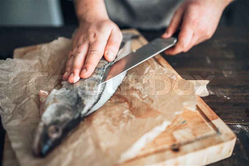Male chef hands with knife cut up raw fish on cutting board, stock photo