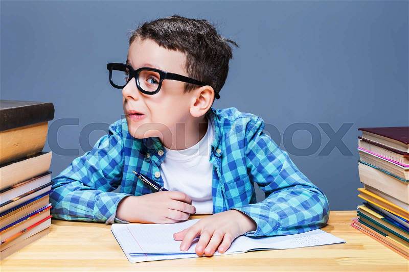 Pupil in glasses squints, bad vision concept. Young schoolboy sitting at the desk against many books, stock photo