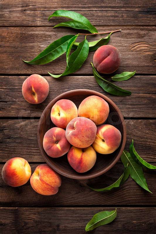 Fresh juicy peaches with leaves on dark wooden rustic background, stock photo