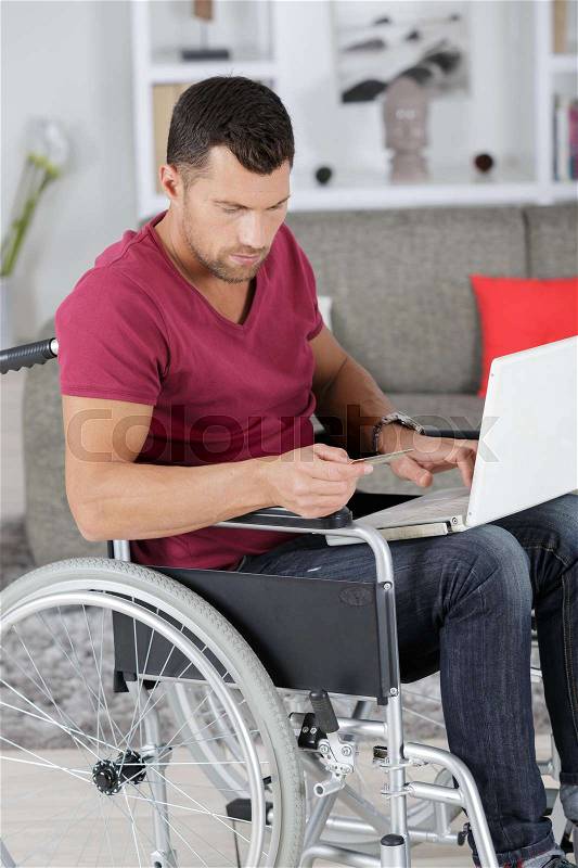 Disabled man in wheelchair typing on laptop, stock photo