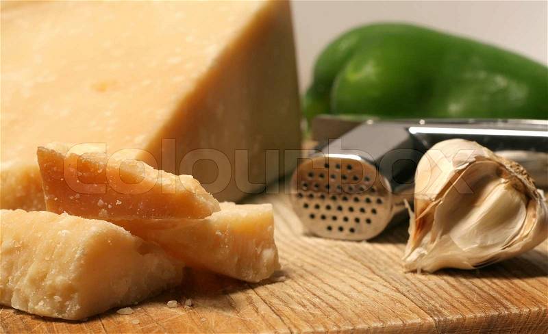 Block of parmesan cheese, green pepper, garlic and press on wooden cutting board, stock photo