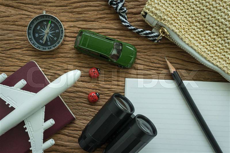 Airplane, passport, compass, binoculars, pencil, paper note and miniature car on wood table as travel planning road trip concept, stock photo