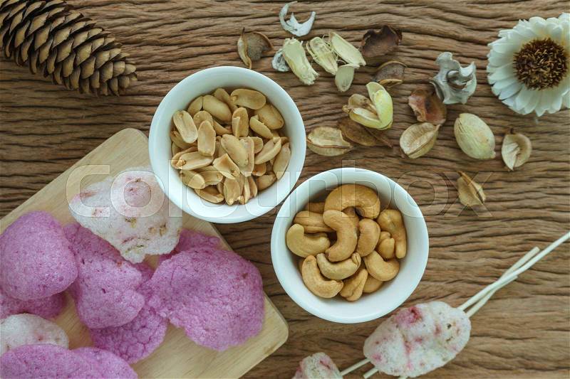 Roasted cashew nuts and peanuts with magenta crisp rice crackers appetizer in white bowl on wooden table, stock photo