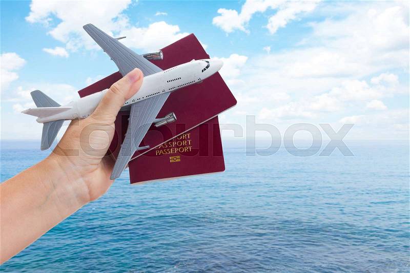 Plane travel concept, hand holding passports with plane over summer sea and sky background, stock photo