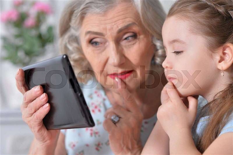 Grandmother with little granddaughter playing in a tablet computer, stock photo