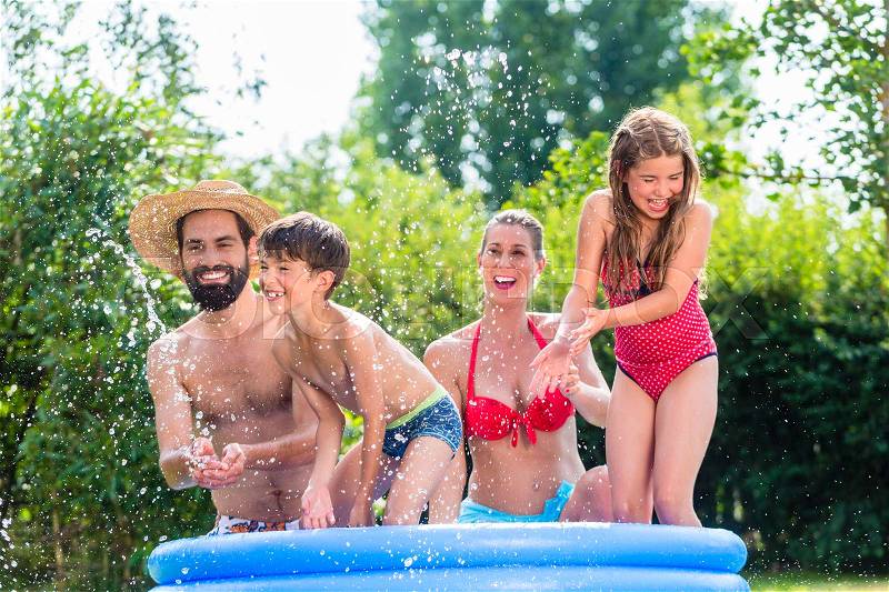 Family in garden pool splashing water cooling down, mother, father and kids having fun together, stock photo