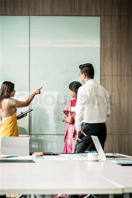 Three creative Indian colleagues writing ideas during brainstorming in the interior of a modern office, stock photo