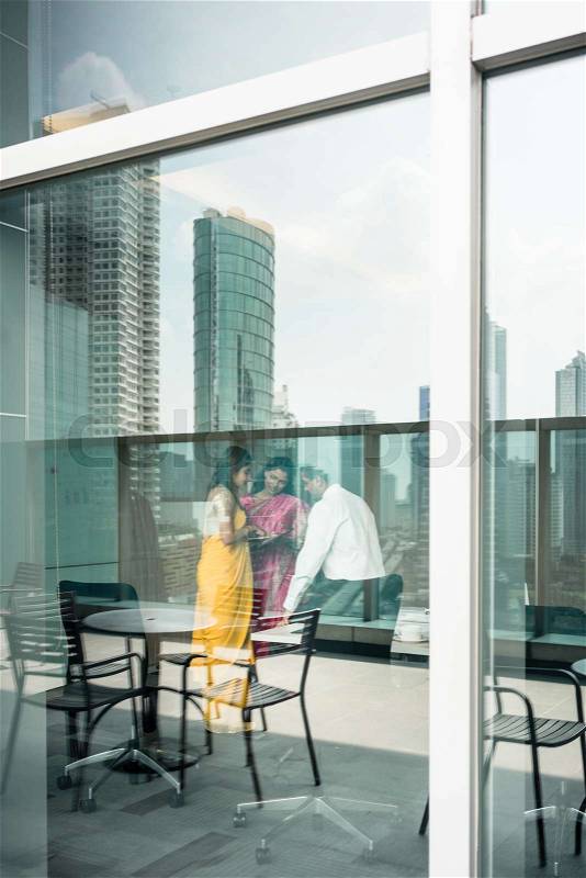 Proficient Indian business people at work in a modern office building with panoramic city view, stock photo