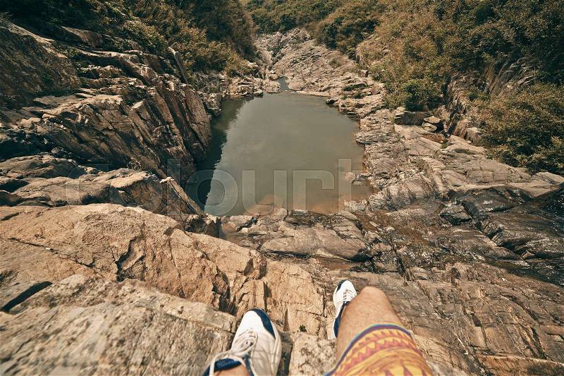 Young brave man sitting on a high stone cliff above little lake. Top view, stock photo