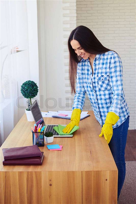 Mid shot of smiling brunette dusting laptop standing on table, stock photo