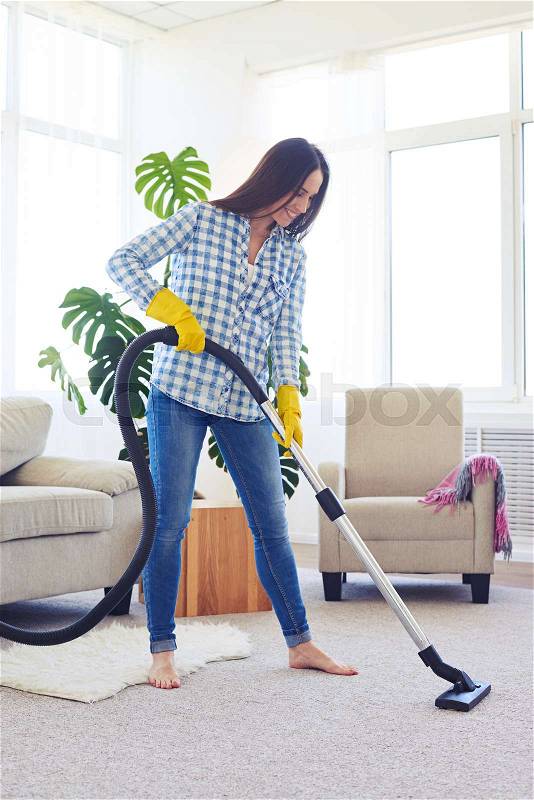 Mid shot of skinny brunette cleaning with vacuum cleaner carpet, stock photo