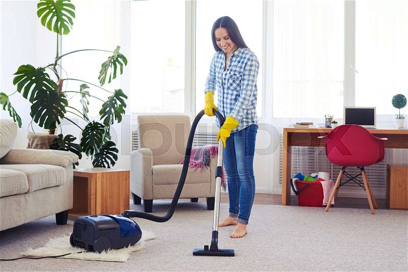 Wide shot of charming housewife cleaning with vacuum cleaner carpet, stock photo