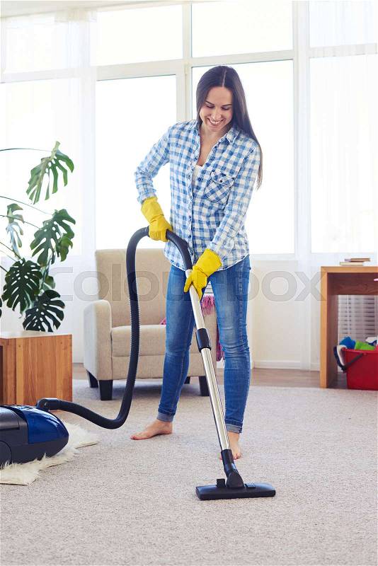 Mid shot of beautiful charwoman cleaning with vacuum cleaner carpet, stock photo