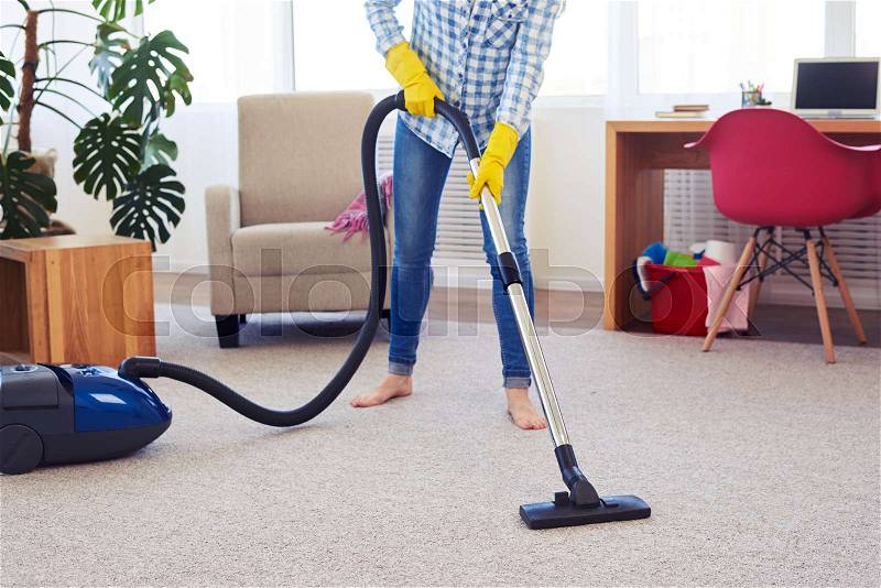 Cropped shot of pretty female cleaning with vacuum cleaner carpet, stock photo