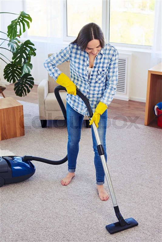 Mid shot of gorgeous woman cleaning with vacuum cleaner carpet, stock photo