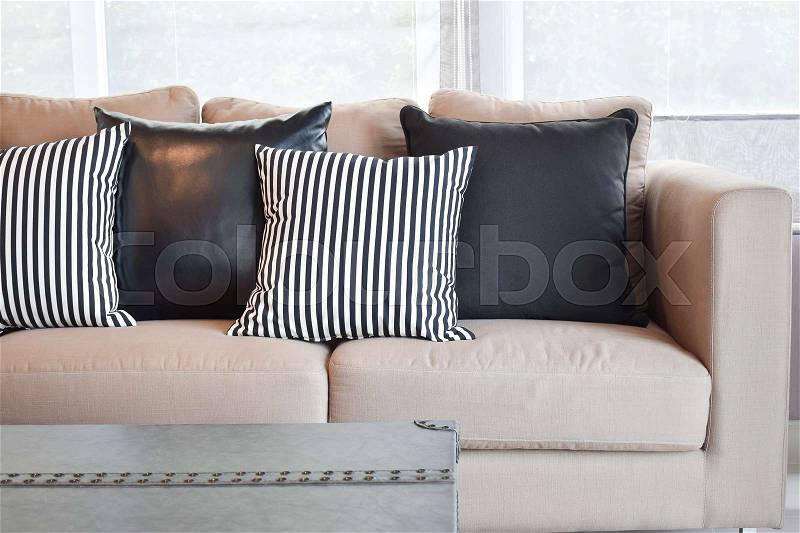 Striped and black leather pillows on velvet beige sofa in modern industrial style living room, stock photo