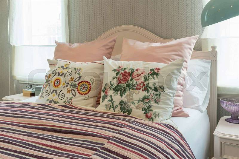 Vintage bedroom interior with flower pillows and pink striped blanket on bed, stock photo
