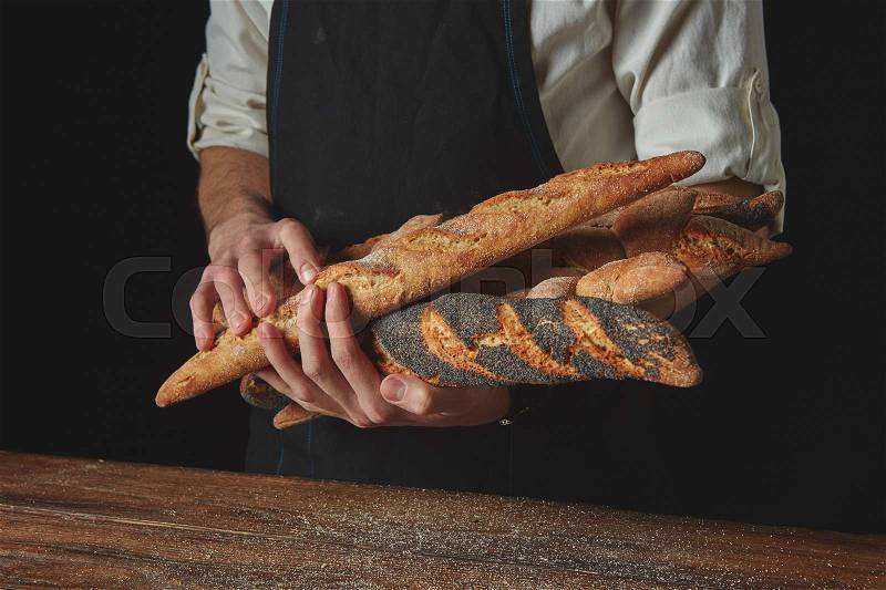 Men\'s hands hold freshly baked baguettes against the black background of a wooden table, stock photo