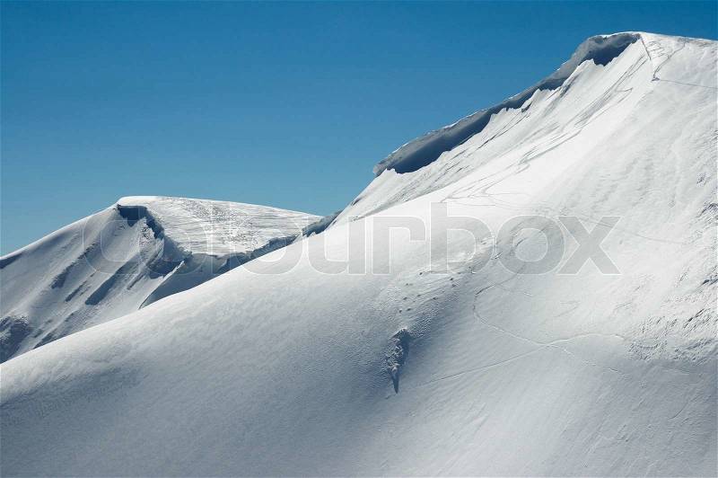 Winter mountains ridge with overhang snow caps and snowboard tracks on blue sky background (Ukraine, Carpathian Mt\'s, Svydovets Range, Blyznycja Mount, Drahobrat ski resort), stock photo