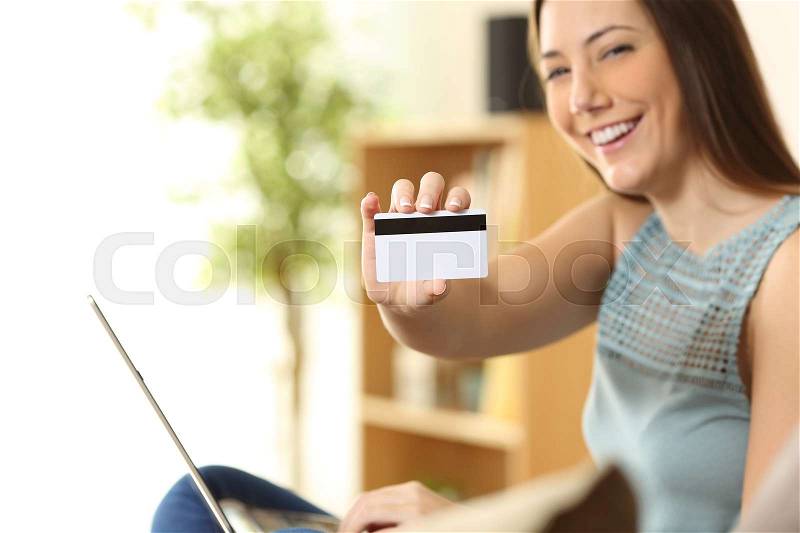 Girl buying on line and showing a blank credit card sitting on a couch in the living room at home, stock photo