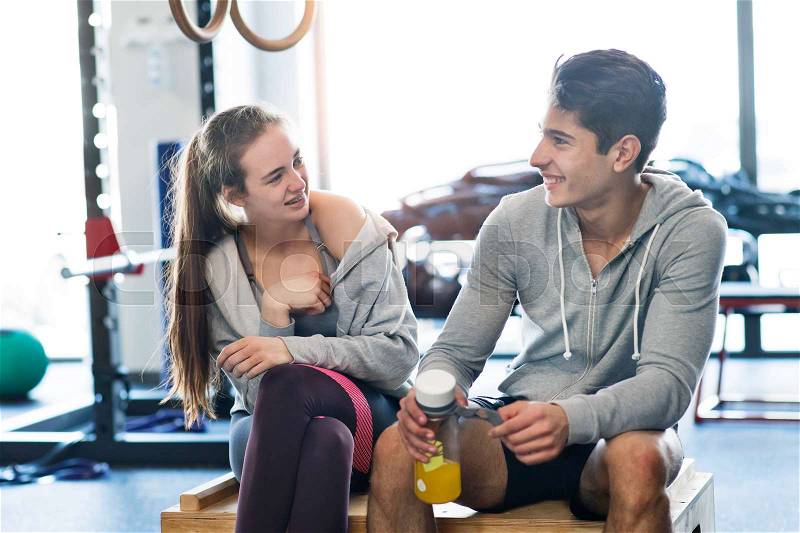 Beautiful young fit couple in modern crossfit gym talking, resting, drinking water, stock photo