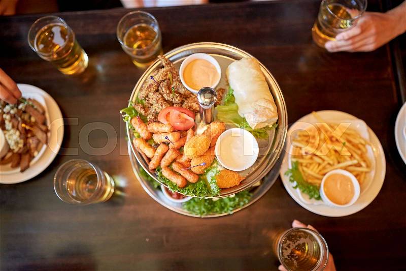Food, drinks and holidays concept - people table with food and beer glasses at bar or pub, stock photo