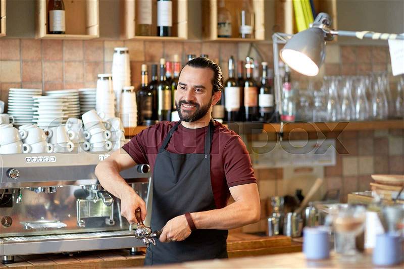 Small business, people and service concept - happy man or waiter in apron with holder and tamper preparing espresso at coffee shop, stock photo