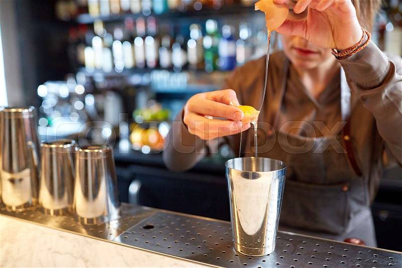 Alcohol drinks, people and luxury concept - woman bartender with shaker braking egg and preparing cocktail at bar, stock photo