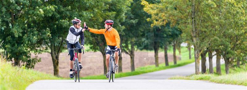Racing cyclists after sport and fitness workout giving high five in finish, stock photo