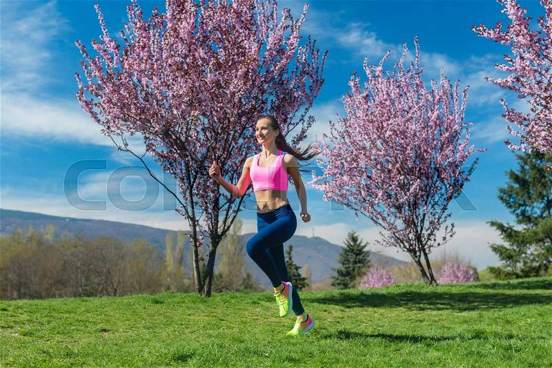 Woman doing sport running on hill between cherry trees blossoming, stock photo