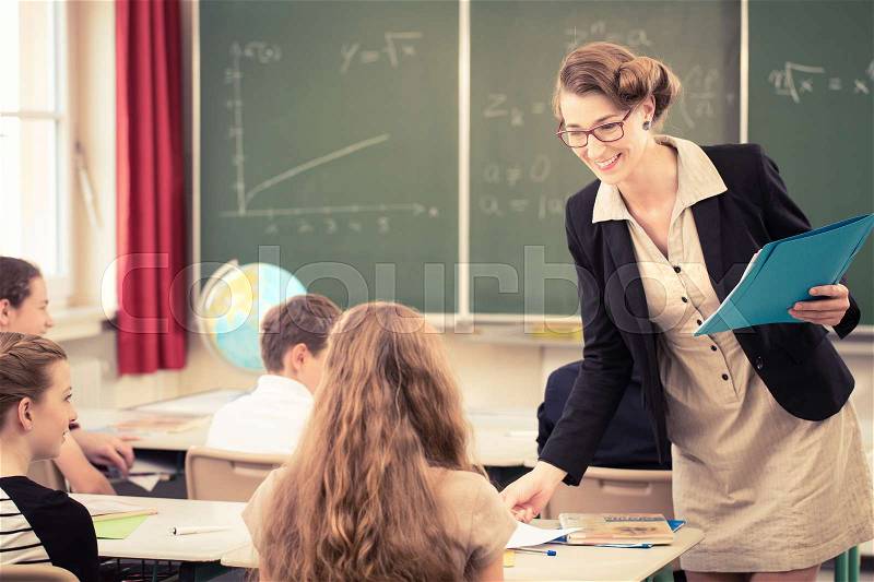 Teacher handing out class work to her students, stock photo