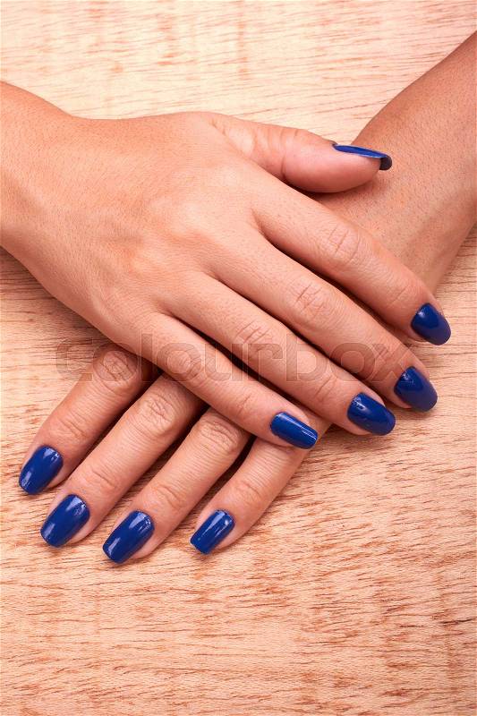 Woman hands and nails blue care of manicure in wood background, stock photo